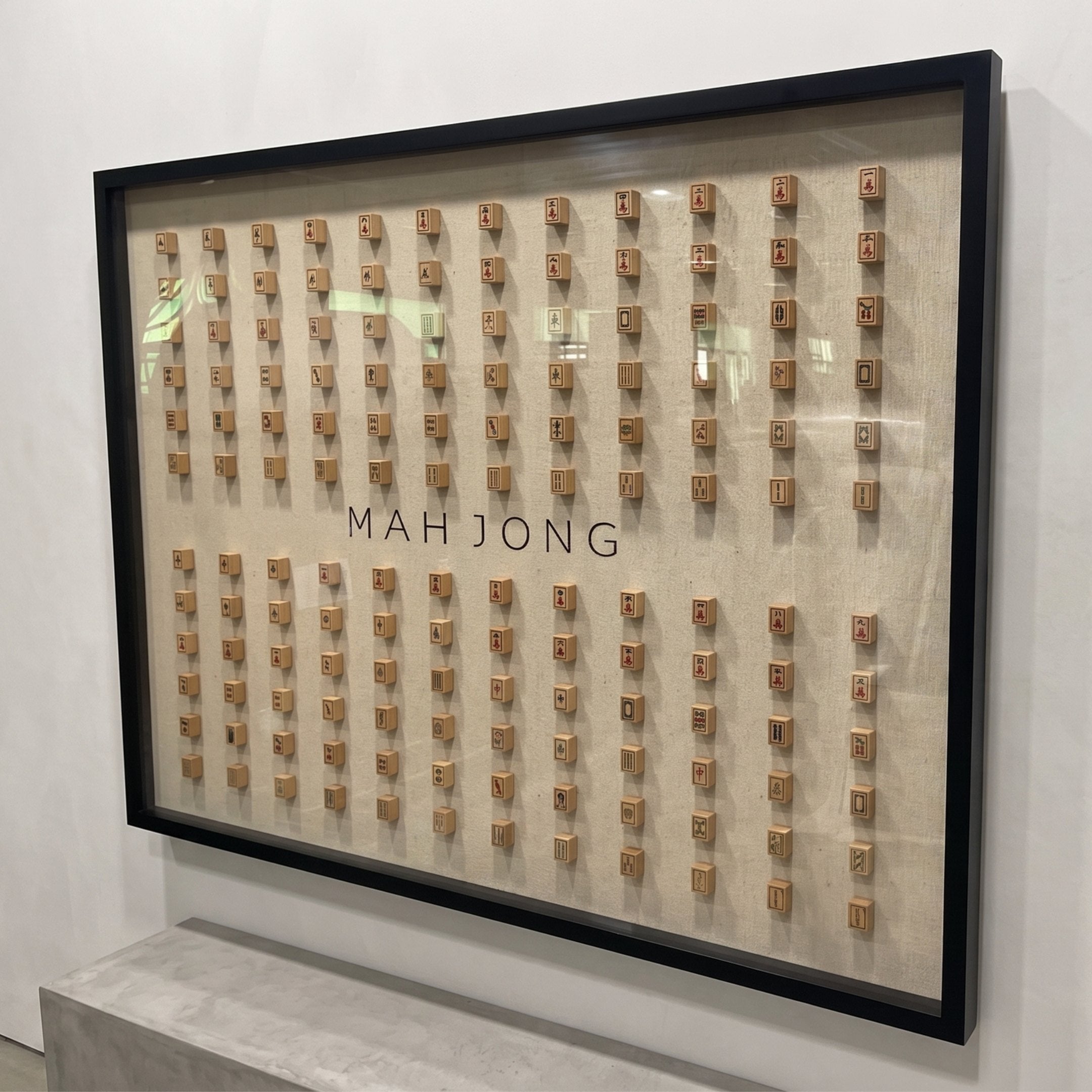Angled view of the Fortuna Mahjong Carved Wood Tile Linen Wall Art by Giant Sculptures, showing the depth of the black frame and the projection of the mahjong tiles from the linen panel.