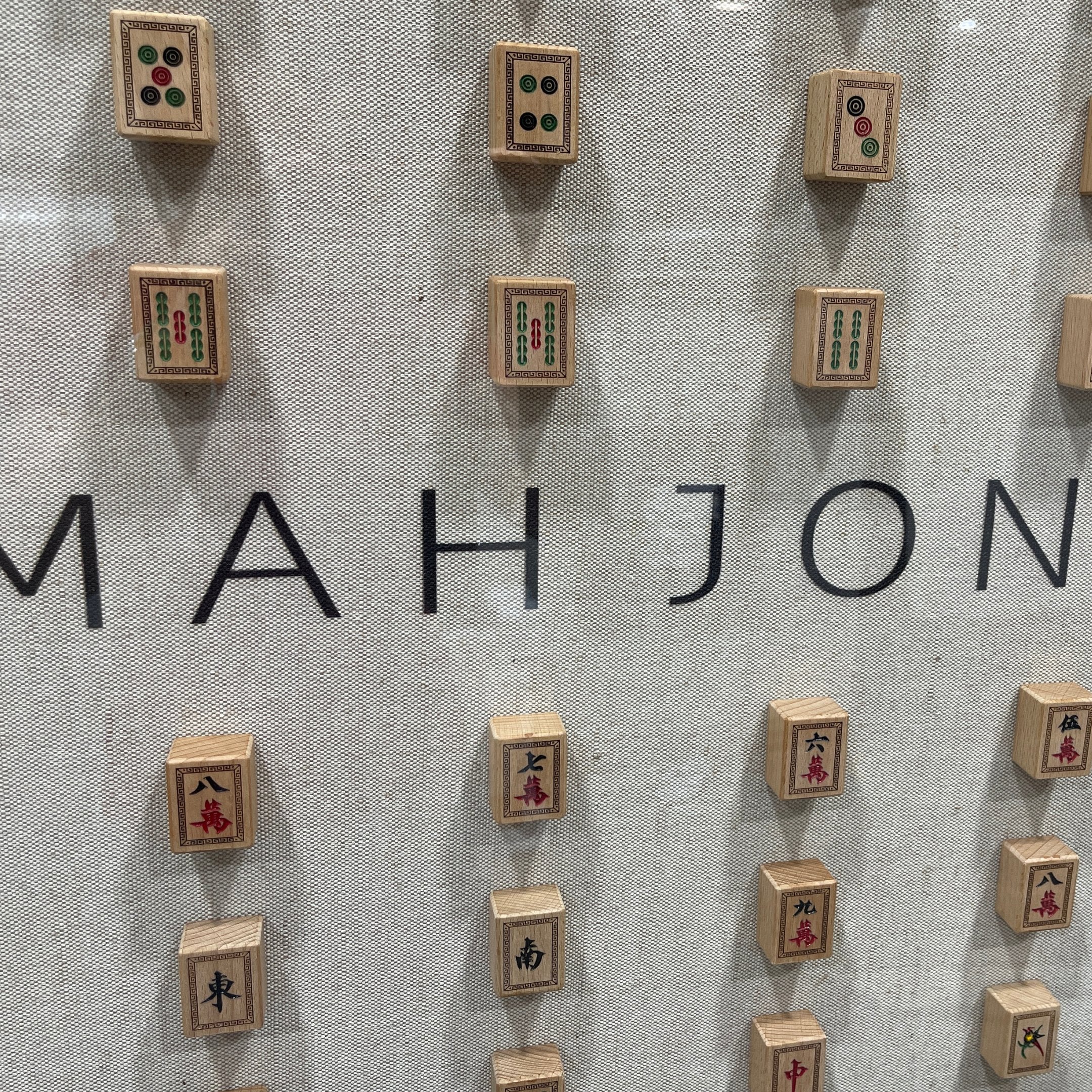 Close detail of the MAH JONG lettering and surrounding carved wooden tiles on the linen ground of the Fortuna wall art, showing the red and green colour work on the individual tile faces.