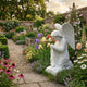 Praying Angel Marble Outdoor Sculpture by Giant Sculptures, a 70cm white marble kneeling angel with clasped hands and detailed wings, displayed in a walled cottage garden among colorful flowers.