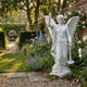 Classic Angel Marble Outdoor Sculpture - 180cm by Giant Sculptures, a white marble winged angel in flowing robes with one arm raised, displayed in a walled English garden with flowers.