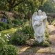 Giant Sculptures Floral Cross Marble Angel Sculpture in white marble, 180cm tall, holding a floral cross, set in a walled English garden with flowering borders.