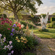 Giant Sculptures Winged Siren Angel Marble Outdoor Sculpture in white marble, 120cm, displayed in a walled English garden with mixed perennial flower borders and a gravel path.