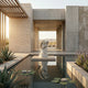Sitting Angel Marble Outdoor Sculpture by Giant Sculptures, 50cm white marble cherub with wings and hands clasped in prayer, displayed on a pedestal over a reflecting pool in a desert courtyard setting.