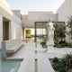 Four Season Angel Marble Outdoor Sculpture by Giant Sculptures, 200cm white marble figure in classical drapery holding grapes on a pedestal in a modern courtyard with olive trees and a water feature.