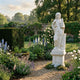 Four Season Angel Marble Outdoor Sculpture by Giant Sculptures, 200cm white marble figure in classical drapery holding a vessel, displayed on a pedestal in a lush walled garden with flowering borders.