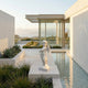 Giant Sculptures Cherub V3 Angel Marble Outdoor Sculpture in white natural marble, 80cm, standing on a stone platform beside a reflective pool in a modern courtyard with succulents and ocean views.