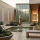 Four Season Female Angel Marble Outdoor Sculpture in warm two-tone white and golden marble, standing on a pedestal in a reflecting pool within a modern courtyard with succulents and glass walls.