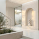Kneeling Woman Praying Angel Marble Outdoor Sculpture by Giant Sculptures displayed in an arched wall niche within a modern cream-toned entryway with stairs and greenery.