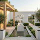Man Angel Marble Outdoor Sculpture by Giant Sculptures, 150cm white marble male angel on a pedestal beside a reflective water feature in a landscaped courtyard garden.