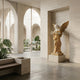 Gold Winged Roman Angel Marble Outdoor Sculpture by Giant Sculptures, 180cm tall, depicting a violin-playing angel in white and golden marble, set in a travertine alcove with arched courtyard behind.