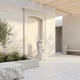 Kneeling Praying Angel Marble Outdoor Sculpture by Giant Sculptures, 80cm white marble figure in prayer pose on a pedestal, set in a sunlit stone courtyard with greenery and a bench.