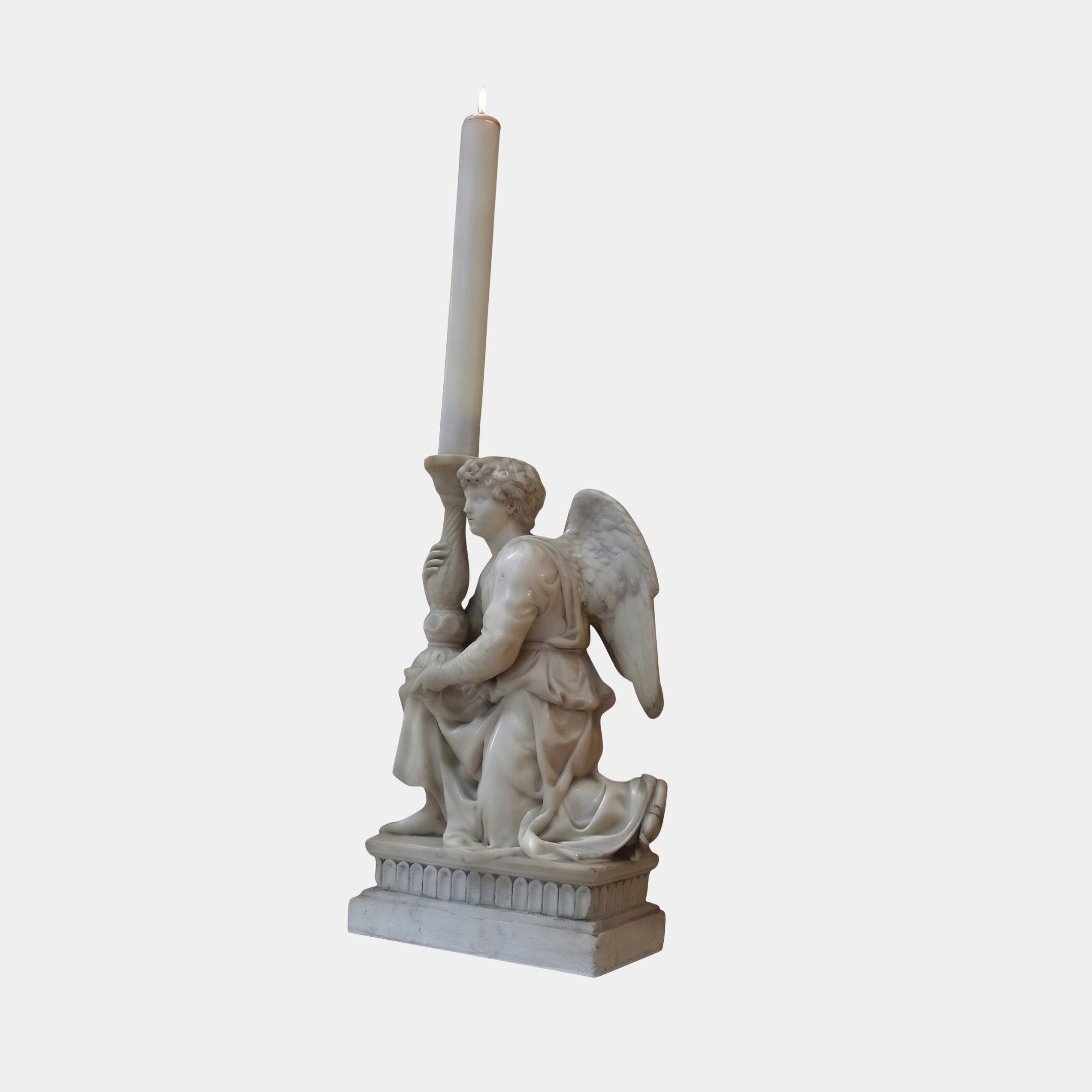 Kneeling Angel With Candlestick Marble Sculpture by Giant Sculptures, depicting a winged angel in flowing drapery holding a tall lit candle, on a fluted base, plain light background.