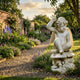 Seated Cherub Angel Marble Outdoor Sculpture by Giant Sculptures, 60cm white marble Puck figure cross-legged on a mushroom base, shown in a walled cottage garden.