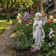 Little Girl Angel Marble Outdoor Sculpture by Giant Sculptures, 80cm white marble cherub in a praying pose with feathered wings, set in a walled cottage garden border with colorful flowers.