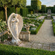 Life-Size Female Angel Marble Outdoor Sculpture by Giant Sculptures, 160cm white marble figure in contrapposto pose with feathered wings, displayed in a formal garden with boxwood hedges and roses.
