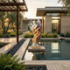 Beige Onyx Angel Marble Outdoor Sculpture by Giant Sculptures, 160cm tall winged angel in flowing golden robes holding roses, displayed on a pedestal beside a reflecting pool in a modern garden.