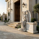 Headstone Memorial Angel Marble Outdoor Sculpture by Giant Sculptures, a seated winged angel carved in white marble on a pedestal, shown beside a stone entrance with lanterns and lavender.