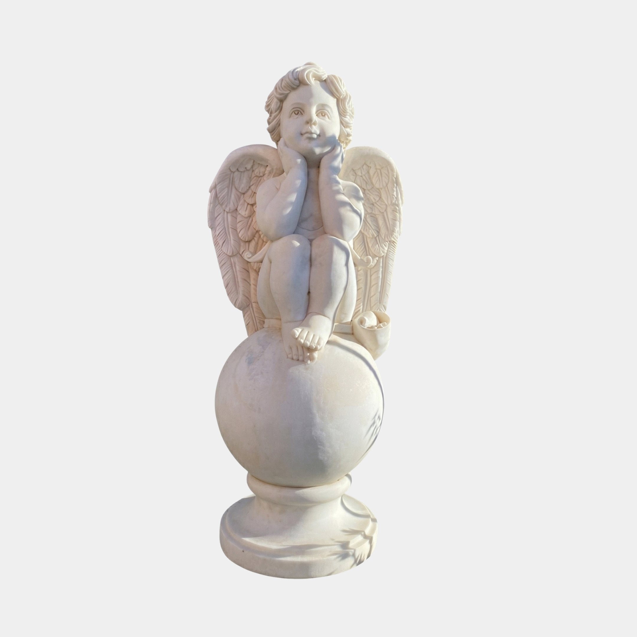 Cherub Angel Marble Outdoor Sculpture by Giant Sculptures, depicting a winged cherub seated on a sphere with hands resting under chin, carved in natural white marble on a round base, against a plain light background.
