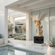 Gold Life-Size Angel Marble Outdoor Sculpture by Giant Sculptures, 225cm tall, depicting a winged angel in flowing robes with white and golden two-tone marble finish on a dark ornate base, displayed poolside in a modern courtyard.