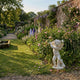 Implacable Putto Cupid Angel Marble Outdoor Sculpture in white marble, shown in an English walled garden setting among roses, foxgloves, and delphiniums.