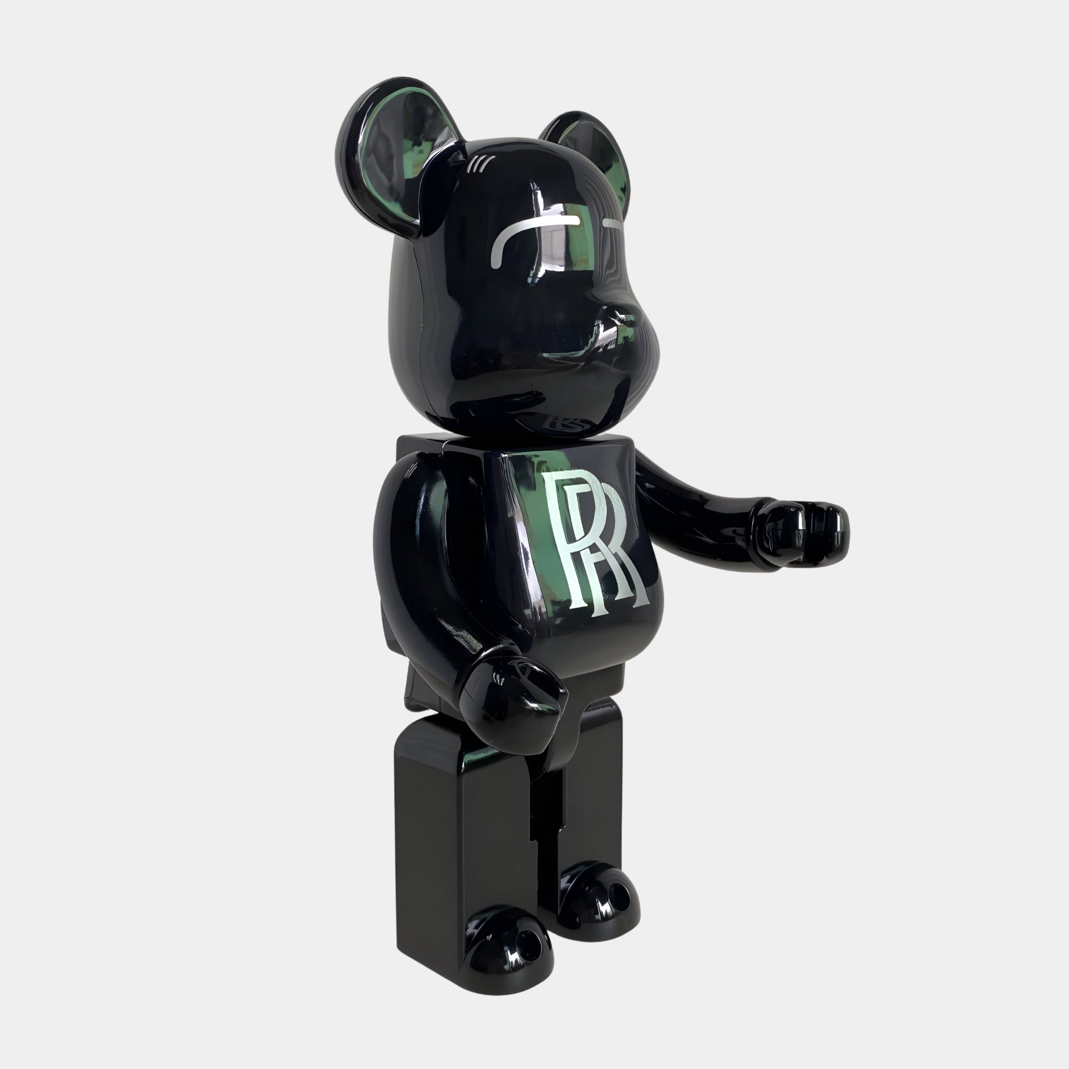 The Midnight Crest Bear Sculpture - 70cm by Giant Sculptures is a glossy black bear figure with a large RR logo on its chest and minimalist features, crafted from piano-gloss resin and posed with one arm raised.