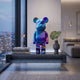 Midnight Sunset Bear Sculpture, 50cm, in blue-purple-orange gradient resin, displayed on a floating shelf with books and a vase in a modern living room.