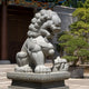 Grey granite guardian lion seated in a temple courtyard under a painted eave