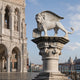 The white marble winged lion on its carved capital beside a paved walk