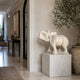 White marble elephant standing in a hall interior beside an olive tree