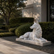 White marble couchant wolf shown on a gravel bed beside clipped hedging