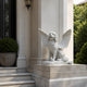 Winged marble dog shown beside a classical stone entrance