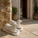 Two white marble sheep shown on paving beside a stone wall