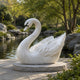 White marble swan on its grey granite disc at the edge of a pond