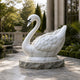 White marble swan on its riven base, shown on a paved terrace