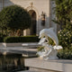 White marble dolphin on its wave, shown on a stone ledge beside a pool