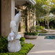 Marble column of three dolphins shown in a planted bed by a pool