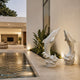 The two leaping marble dolphins lit beside a poolside at dusk