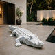 Faceted white marble crocodile lying directly on poolside paving
