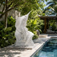 The marble sailfish on a low plinth beside a lap pool, palms behind