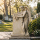 Cream marble angel and stele memorial shown in an older burial ground