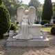 Marble seated angel memorial with flower vases shown on a gravel plot