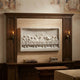 Box-framed stone Last Supper relief hung on a panelled overmantel above an oak sideboard