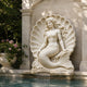 Mermaid scallop shell marble relief shown set against a masonry garden wall above a pool