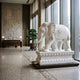 Elephant With a Cloud-Scroll Cloth Marble Statue, 180cm, white marble with carved roundel and tassels, displayed on a base in a lobby near a bonsai plant.
