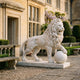 Standing Lion With a Paw on a Sphere Marble - 180cm by Giant Sculptures, cream-white marble lion in profile with paw on sphere, on a flat base outside a stone manor courtyard.