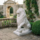 Seated Lion With a Sphere White Marble Statue - 120cm, roaring with paw on sphere, on a stone patio near a bench and archway.