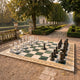 Giant Sculptures' 40cm black and white marble chess set arranged mid-game on a green and cream checkered board in a formal garden with tree-lined path.