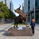 Monumental Charging Bull Bronze Sculpture by Giant Sculptures at 300cm, shown on a granite plinth beside a woman for scale in a modern city plaza.