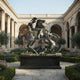 Monumental Classical Armoured Warrior and Dragon Bronze Sculpture by Giant Sculptures on a black plinth in a colonnaded courtyard with hedged garden beds.