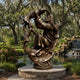 Monumental Classical Bearded Figure with Children Bronze Sculpture, 300cm, in a garden setting beside a pond, showing a bearded bronze figure lifting and surrounded by children in a swirling composition on a round stone base.